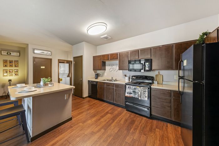 Highlander at North Campus model kitchen with dark wood cabinets, breakfast bar, and warm wood flooring in Riverside CA