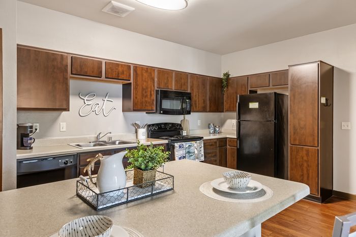 Highlander at North Campus model kitchen with rich wood cabinetry, sleek black appliances, and charming decor in Riverside CA