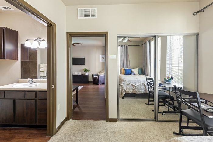 Highlander at North Campus apartment interior with cozy bedroom, mirrored closet, and bright living area with wood flooring in Riverside CA