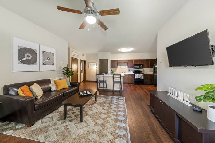 Highlander at North Campus open-concept living room with leather sofa, modern kitchen, and warm wooden flooring in Riverside CA