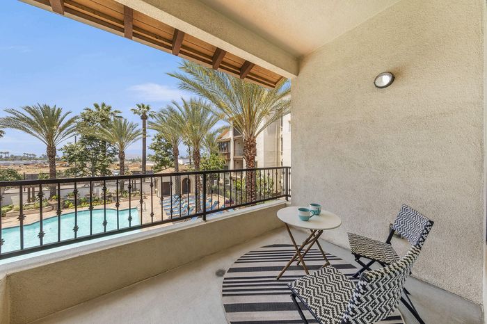 Highlander at North Campus model patio balcony with cozy seating overlooking the sparkling pool and palm trees in Riverside CA