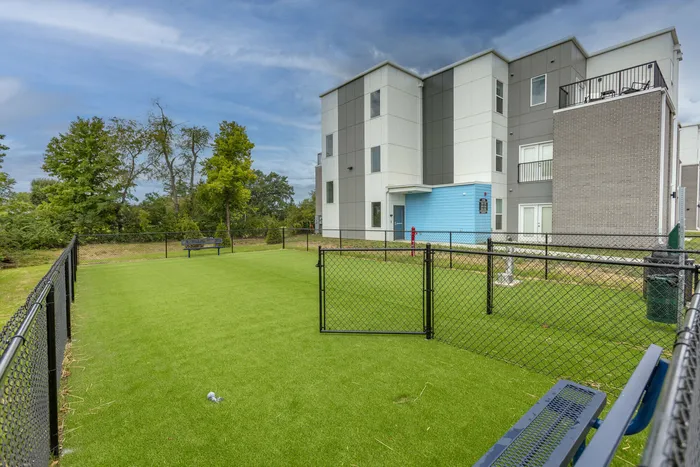 Modern apartment complex with a lush green fenced area, perfect for outdoor activities and relaxation.