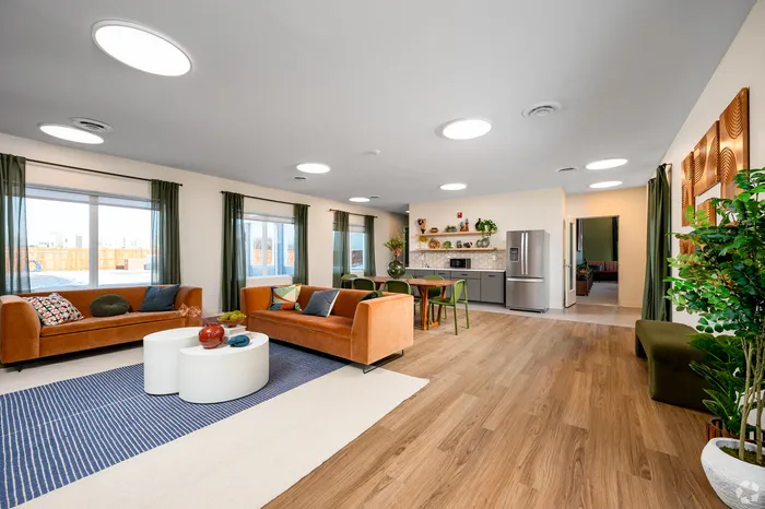 Bright open-concept living room with modern decor, comfortable orange sofas, and fully-equipped kitchen, under soft natural lighting.