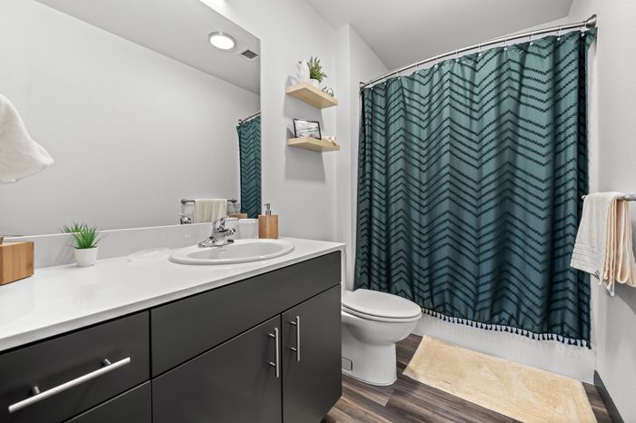 Modern bathroom featuring a sleek vanity, stylish green shower curtain, and chic open shelving, offering elegance and functionality.