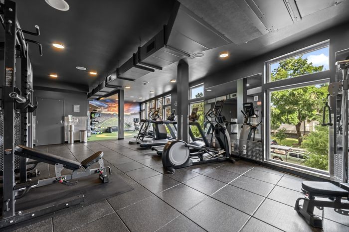 Contemporary fitness center with state-of-the-art exercise equipment, large windows showcasing lush greenery, and a vibrant sports-themed mural.