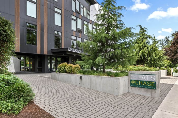 Modern apartment building entrance at The Flats @ Chase, surrounded by lush greenery and sleek architectural design, ideal for contemporary student living.