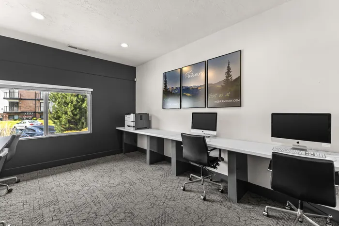 Modern shared workspace with sleek desks, computers, and a large window offering natural light and a view, ideal for productivity.
