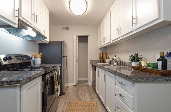 Modern kitchen with sleek granite countertops, white cabinetry, stainless steel appliances, and warm wood flooring, creating a stylish and welcoming cooking space.