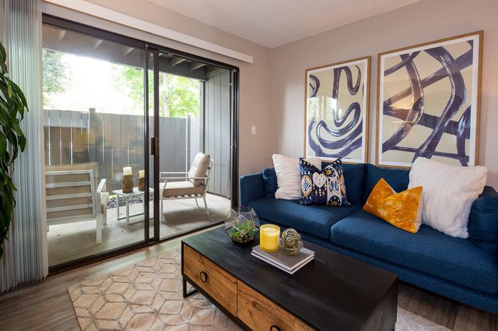 Inviting living room with stylish blue couch, vibrant throw pillows, modern art, and a bright patio view through sliding glass doors.