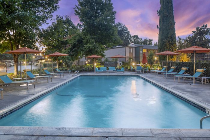 Inviting pool area with lounge chairs and umbrellas, set against a serene evening sky, perfect for relaxation and leisure.