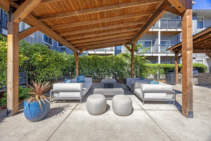 Chic outdoor lounge area in Chase Courtyard apartment complex with cozy seating around a stylish fire pit, featuring a modern pergola and a nearby poolside setting.