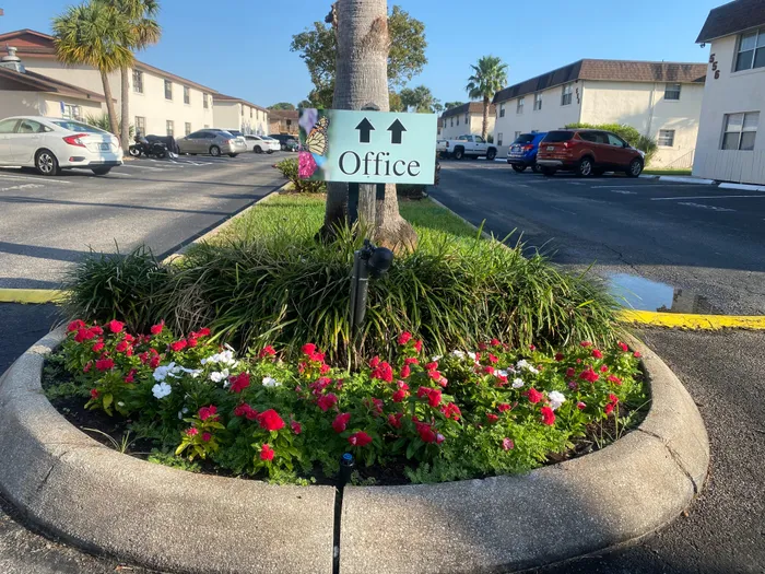 Marcell Gardens Apartments, Sign pointing to office, Flowers in flower bed with trees, stairs