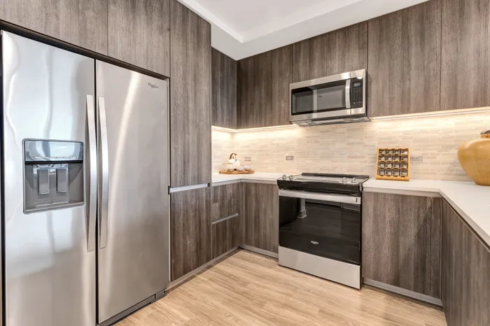 Kitchen with handleless dark wood cabinets, light wood-style floors, stainless steel appliances, and white quartz countertops.