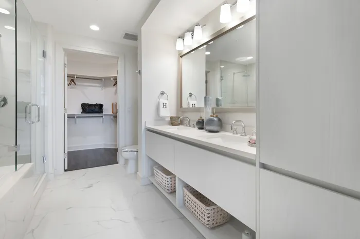 Spacious bathroom with a dual vanity with a white quartz countertop, walk-in closet, white marble tiling, and glass walk-in shower.