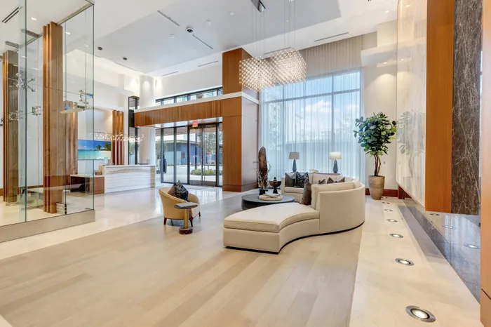 Lobby with a curved couch, wood-paneled and marble-clad walls, high ceilings, window walls, and a concierge desk.