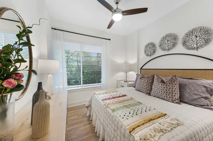 A spacious bedroom with a king-sized bed, ceiling fan, wood-style floors and large window.