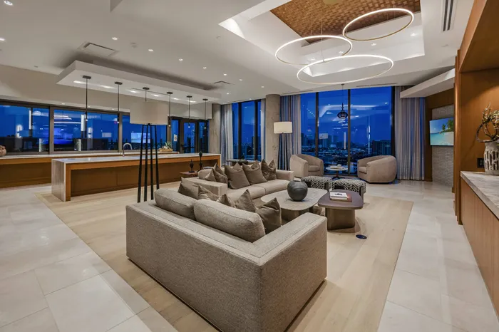 Clubhouse decorated with modern, neutral finishes, a marble dining table with 12 chairs, a seating area with three armchairs and a long couch, and beige carpet.