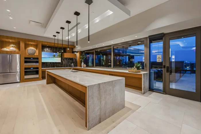 A clubhouse kitchen facing full window walls with a city skyline view. The floors, walls, and columns are marble-clad.