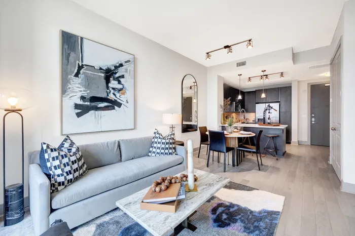 Spacious living and dining areas with warm wood-style floors, floor-to-ceiling windows, a large sofa, and a 4-person round dining table