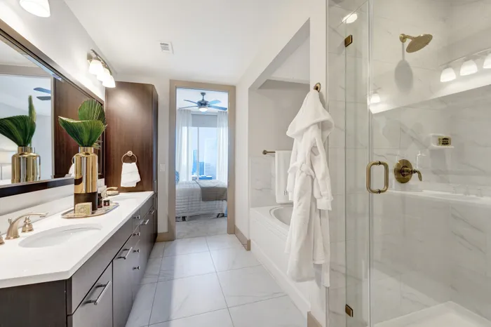 En-suite bathroom with a frameless glass walk-in shower, large bathtub, stone floors, and stone-topped dual vanity