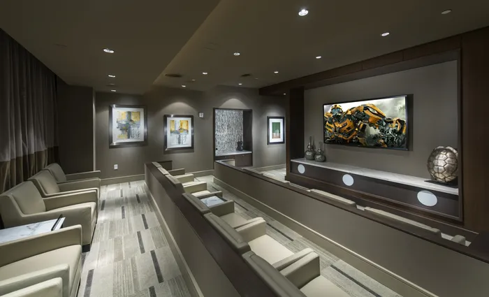 Large, low-lit media room with three terraced rows of large leather armchairs and a blackout curtain along the back wall