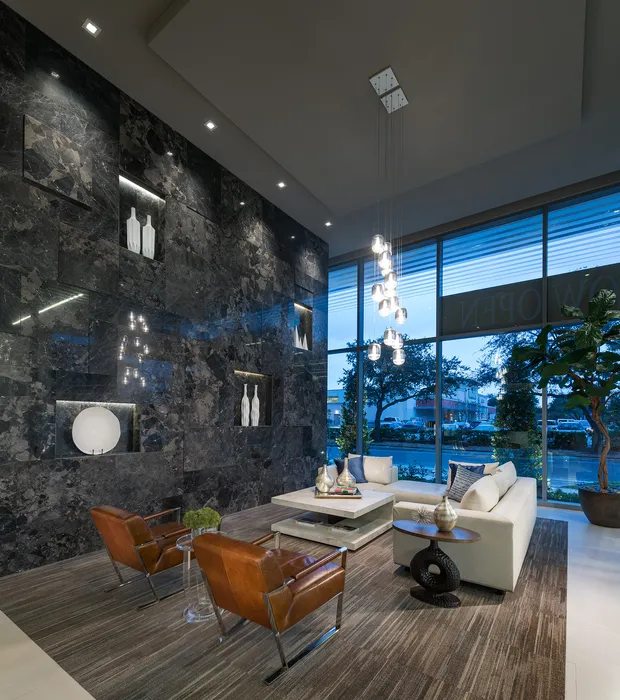 Lobby seating area with high ceilings, floor-to-ceiling windows, a white leather sectional, and leather armchairs next to a full-height black marble accent wall with white vases placed into alcoves