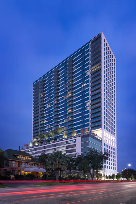 High-rise apartment with balconies and an 8th-floor rooftop pool deck with palm trees viewed from down the street