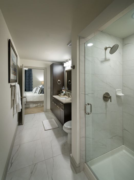 En-suite bathroom with a frameless glass walk-in shower, marble tile on the floor and shower walls, and dark wood cabinetry