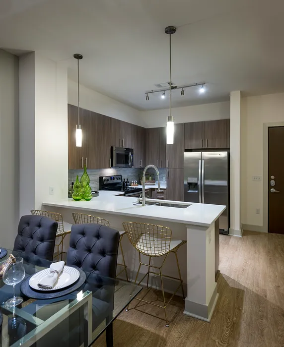 A kitchen with dark wood-style cabinets, stainless steel appliances, and a white quartz peninsula with 3 bar stools.