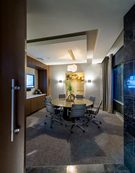 Modern conference room with a round table, 8 rolling chairs, a 70' presentation TV, large windows with curtains and a recessed ceiling.