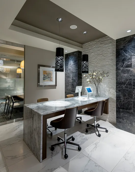 Four rolling chairs at a marble desk with two small touchscreen displays.