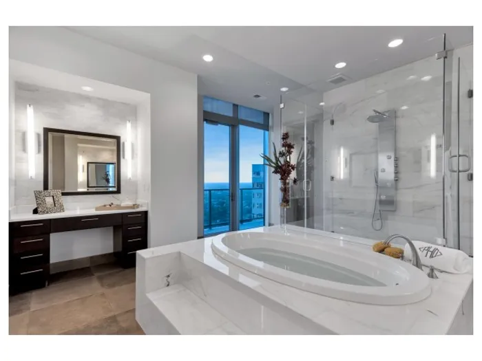 Vast bathroom with a marble-clad step-up oval bathtub, large frameless walk-in shower, and sliding door out to a balcony