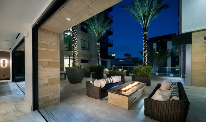 Outdoor firepit and lounge area adjacent to the indoor clubhouse with full-length windows that slide away to create an indoor-outdoor space. There are two wicker couches on opposite sides of the firepit.