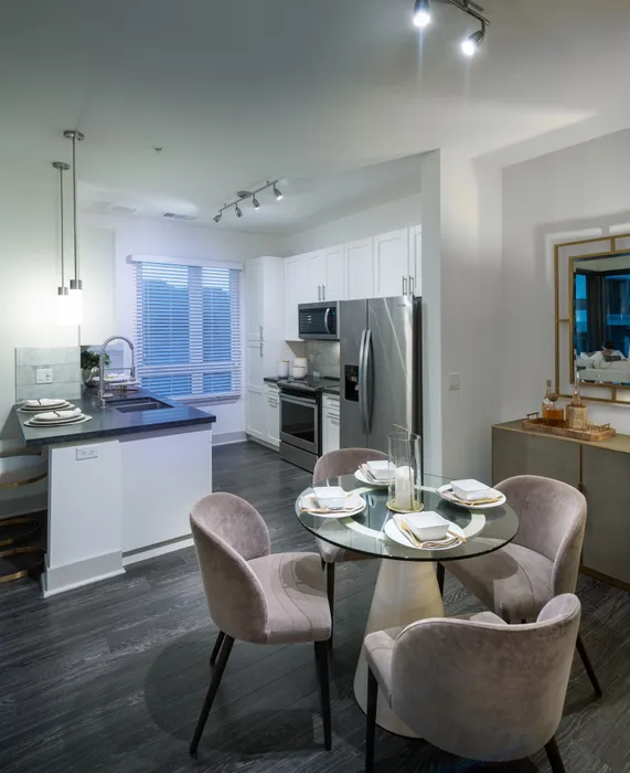 Open-concept kitchen and 4-person dining room with dark wood-style floors, white cabinets, stainless steels appliances, and dark granite countertops.