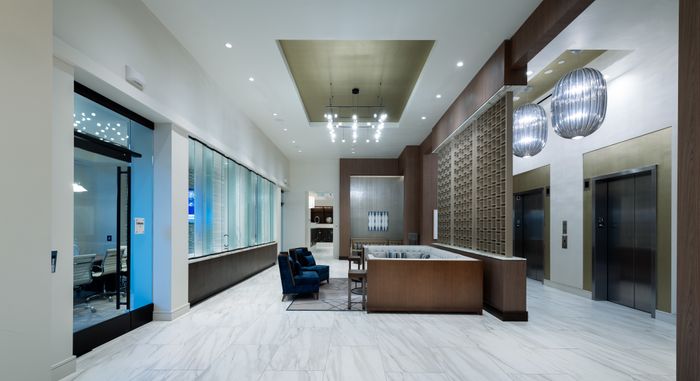 Seating area between an elevator bank and a glass-walled conference room, with armchairs and a large banquette couch.