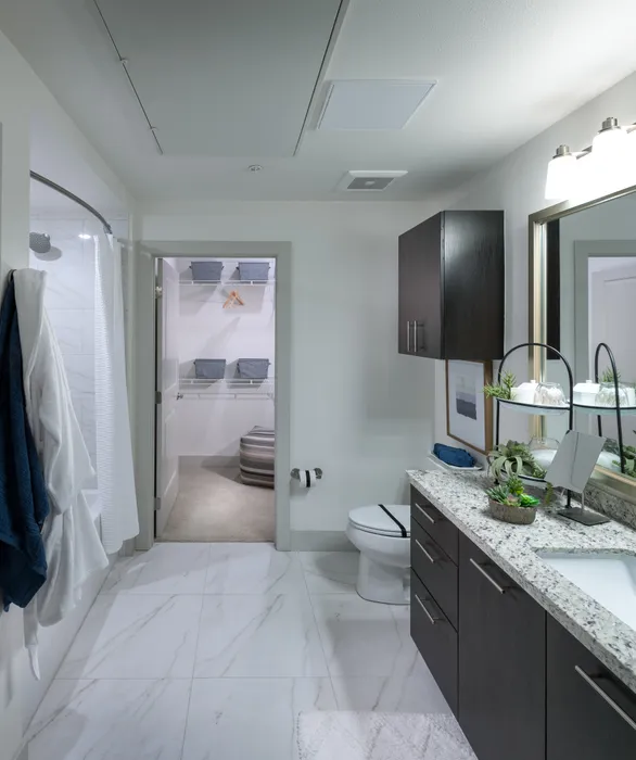 Spacious bathroom with marble floors, a bathtub with a shower curtain, dark wood cabinets, granite countertops, and a carpeted walk-in closet.