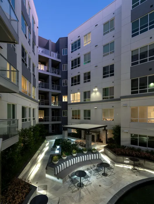 A courtyard surrounded by the interior walls of the apartment complex, with balconies overlooking the landscaping, patio tables and chairs, and dining cabana.