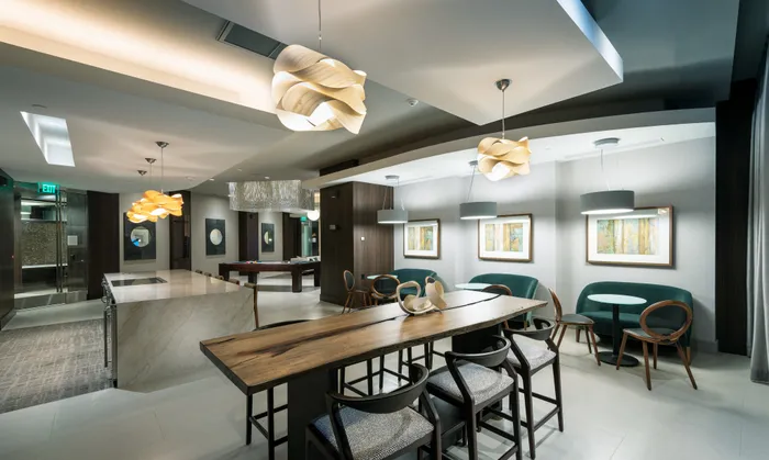 Resident catering kitchen with barstools at a large marble island, cafe-style seating along the wall, and a 6-person wood dining table.