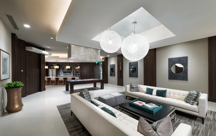 Clubhouse with dark wood-paneled walls, a pool table, two long white couches around a coffee table, and a resident catering kitchen with a wet bar.