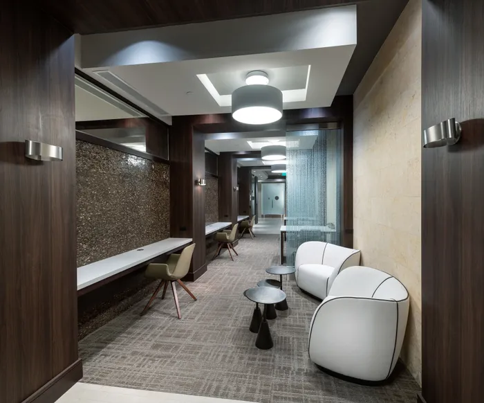 A carpeted hallway-like work area furnished with armchairs, two-person tables, and a desk along the wall with outlets.