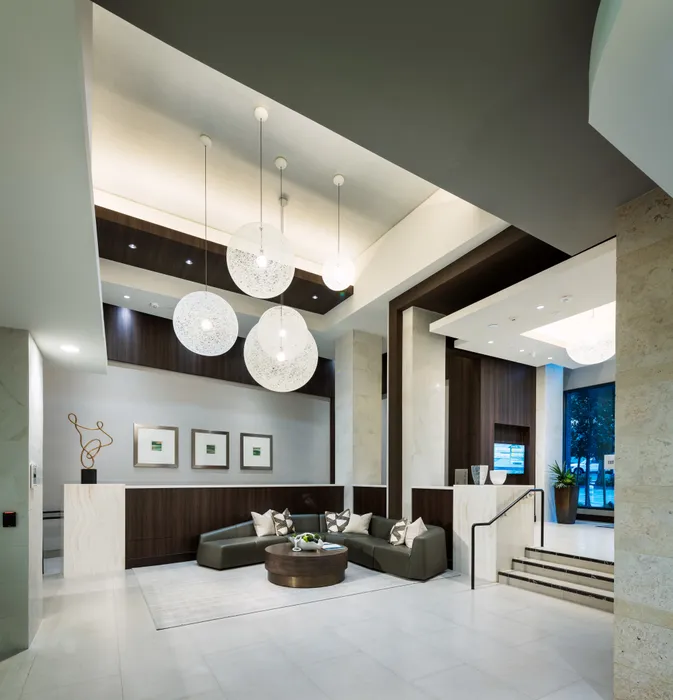 Spacious lobby with high ceilings, a modern globular chandelier, marble floors, a concierge desk, and a curved couch around a coffee table.