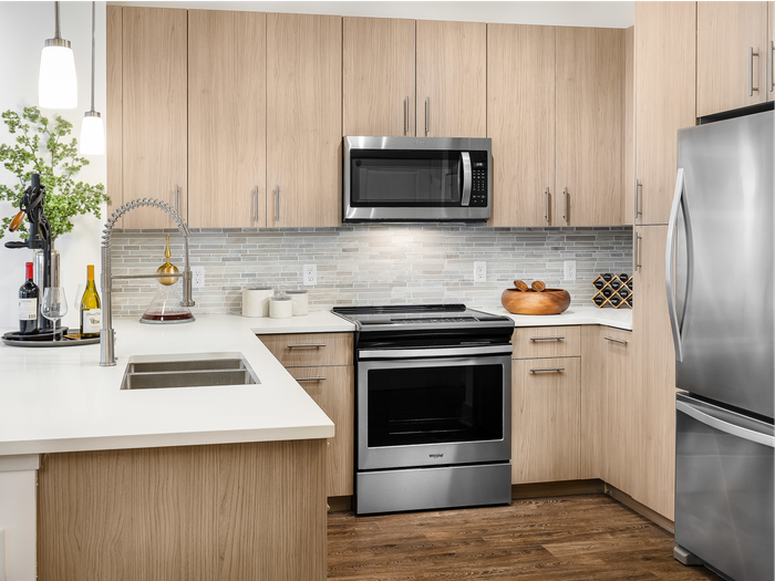 Kitchen with light wood cabinetry, stainless steel appliances, dark wood-style floors and modern light fixtures.