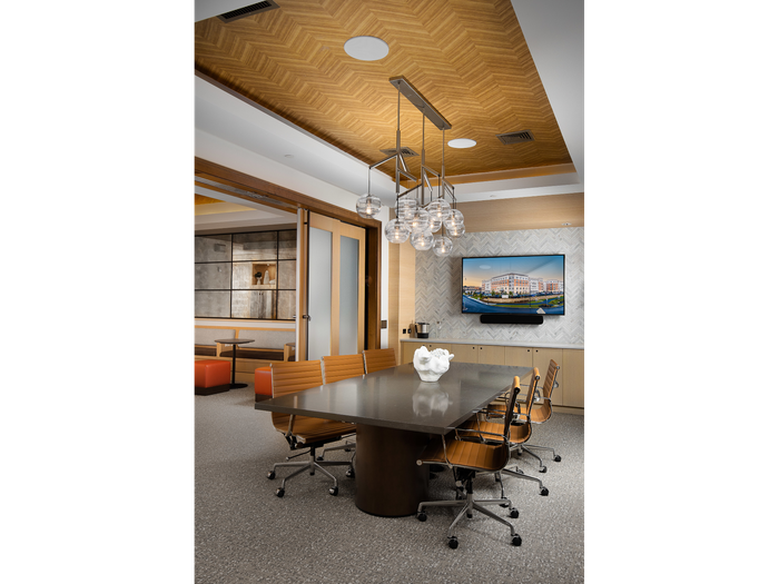 Private conference room with opaque glass sliding doors, a marble conference table with 6 rolling chairs, an HDTV and modern light fixtures.