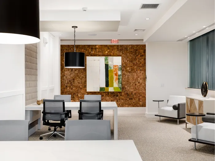 Two workstations in the E-lounge with white desks, gray and black rolling chairs and two leather seats with tables attached.