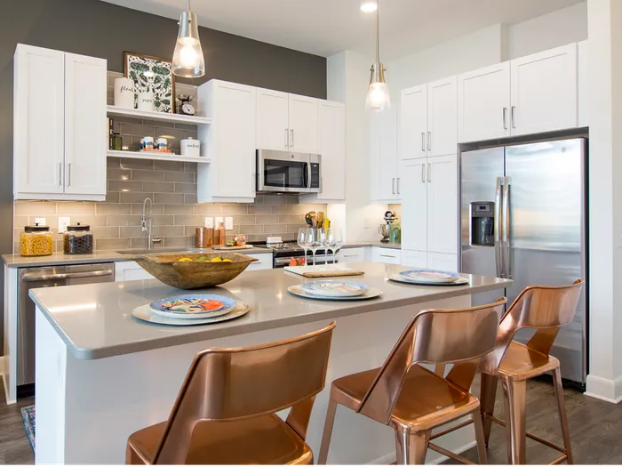 A bright kitchen with stainless steel appliances, white cabinets, built-in shelves, dark wood-style floors, and an island with three barstools.