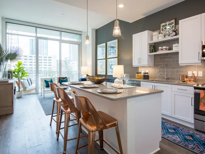 An spacious open-concept kitchen and living space with white cabinets, dark wood-style floors, and full-width floor-to-ceiling windows.