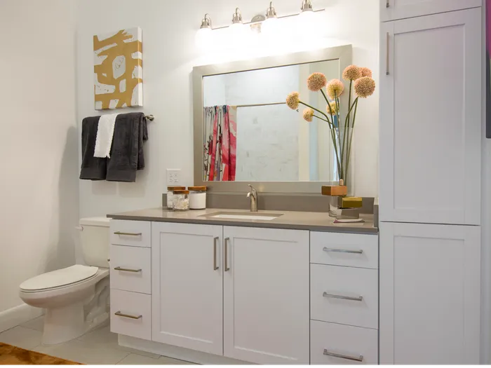 A bathroom vanity with a quartz countertop, white cabinets and drawers below the sink, and cabinets up to the ceiling beside the vanity.