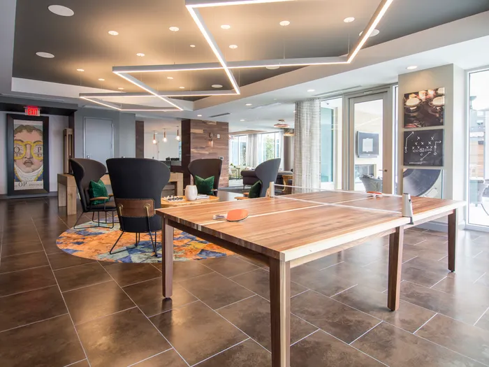 A lounge space with a ping pong table, four chairs around a coffee table, large windows, and colorful, angular modern art.