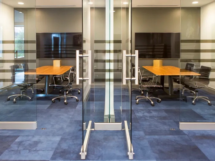 Two glass-walled conference rooms, each with a large HDTV on the wall and four rolling leather chairs around a conference table.