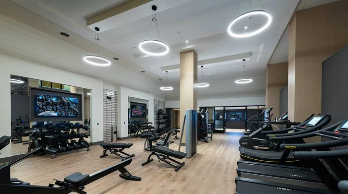 Gym with cardio equipment, weight machines, dumbbells, kettlebells, benches, multiple HDTVs, and wood-style floors